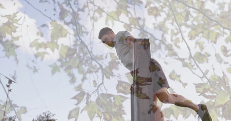 Performing dips man wearing sportswear on parallel bars at outdoor park with tree branches, leaves