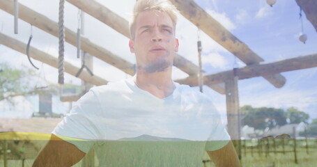 Gazing athlete wearing white T-shirt under wooden horizontal bars in park with gymnastic rings