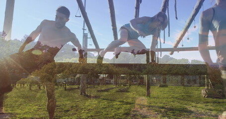 Training fitness partners navigating wooden obstacle course in grassy field, with hanging ropes