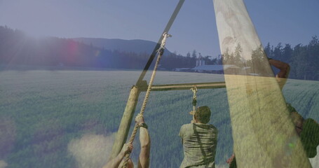 Climbing obstacle frame in green field wearing gloves and straps gripping thick ropes, barn silos © vectorfusionart