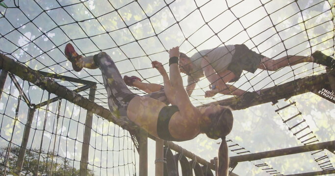 Climbing fit friends navigating cargo net on obstacle course, with wooden beams, metal ladder rungs