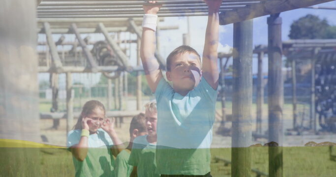 Reaching boy wearing light blue tee grabbing monkey bars at playground, wooden posts and wristband