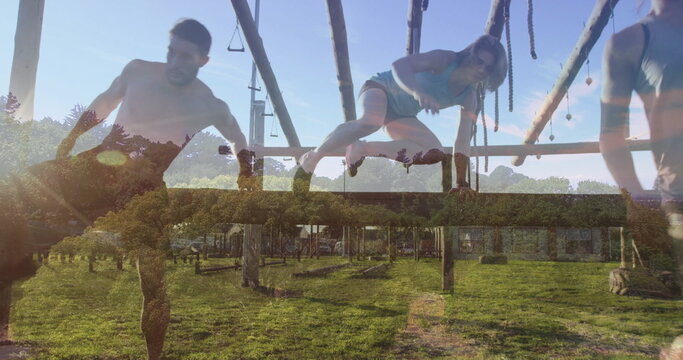Fototapeta Training fitness partners navigating wooden obstacle course in grassy field, with hanging ropes