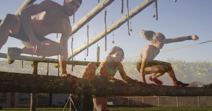 Navigating shirtless man and women in sportswear on wooden beam in outdoor course with ropes - Powered by Adobe