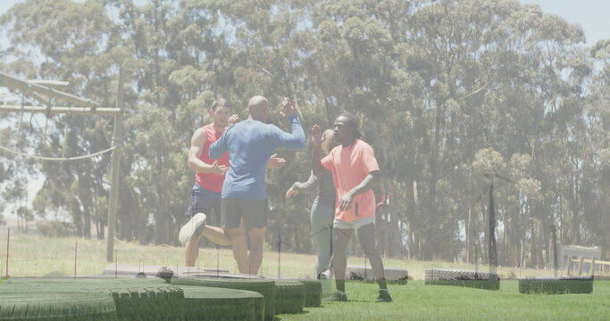 Fototapeta Celebrating group of four adults exchanging high fives on grassy training field, with stacked tires