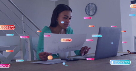 Reviewing mid-age woman examining chart sheet, glancing laptop in home office with digital overlays