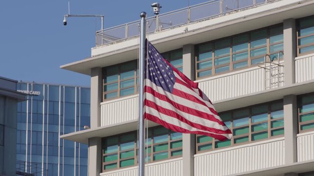 Slow motion of American flag fluttering in the wind in street, with modern glass building background on sunny day