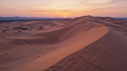 An expansive desert with rolling golden sand dunes under a vibrant sunset sky, soft shadows creating wavy patterns on the dunes, small tufts of desert grass scattered sparsely - Powered by Adobe