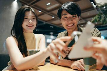 A young couple taps their smartphone to complete a contactless payment at a café-style workspace,...