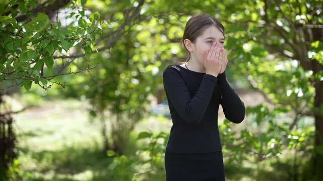 Sick teenage girl coughs in park covering mouth with hand. Unwell young female adolescent coughs in outdoor space shielding mouth with palm. Vulnerable and uncomfortable illness kid