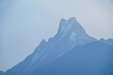 Snow-capped Mount Machhapuchhre peaks visible in the morning with mist and ray of light at Annapurna Base Camp, Nepal.