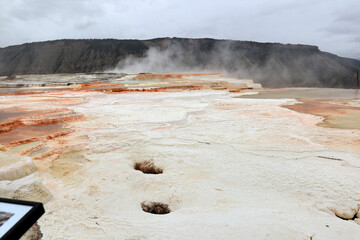 Mammoth terraces in Yellowstone. A large hill of red-brown color from which steam rises. A mountain...