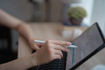 Businesswoman using stylus pen pointing on digital tablet screen while working and analyzing financial charts and graphs showing changes on the market