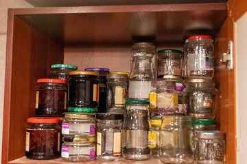 Many empty and full glass jars stacked in kitchen cabinet