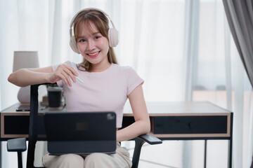 Asian freelancer woman working remotely in her home office, using a digital tablet and stylus pen...