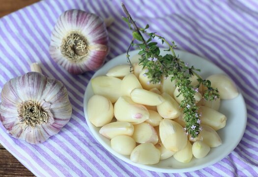 Freshly peeled garlic cloves and thyme on the small plate. Top view of garlic cloves and bulbs on the table.