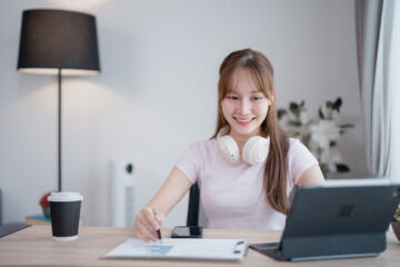 Young Asian business woman with headphones around her neck smiling and working from home using...