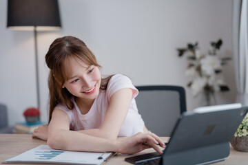 Smiling businesswoman working remotely from a modern home office, using a tablet to analyze...