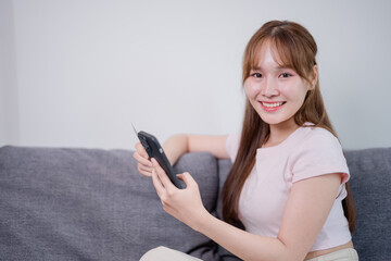 Smiling young asian woman is making online payment holding credit card and using smartphone while...