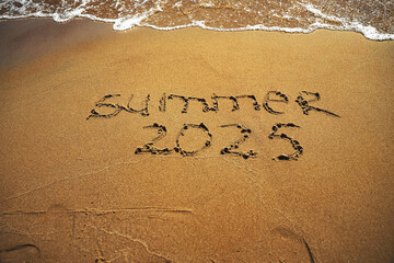 Hand drawn message Summer 2025 on wet yellow sand on beach of sea