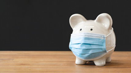 Worried piggy bank wearing a protective face mask symbolizes financial uncertainty and the impact of global health crises on savings and investments