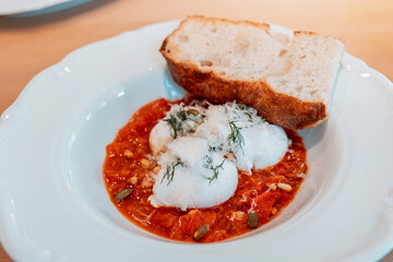 Delicious breakfast with poached eggs in tomato sauce with herbs, parmesan, seeds and toasted bread served in a white plate