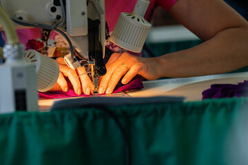 Zoom sur une machine à coudre en fonctionnement avec des mains en pleine action guidant le tissu, illustrant le geste précis de la confection artisanale.