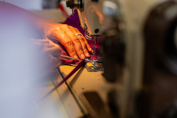 Zoom sur une machine à coudre en fonctionnement avec des mains en pleine action guidant le tissu, illustrant le geste précis de la confection artisanale.