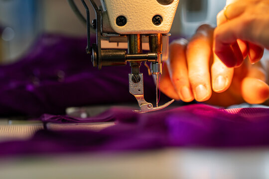 Zoom sur une machine &agrave; coudre en fonctionnement avec des mains en pleine action guidant le tissu, illustrant le geste pr&eacute;cis de la confection artisanale.