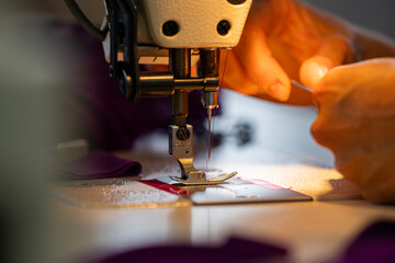 Zoom sur une machine à coudre en fonctionnement avec des mains en pleine action guidant le tissu, illustrant le geste précis de la confection artisanale.