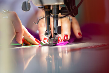 Zoom sur une machine à coudre en fonctionnement avec des mains en pleine action guidant le tissu, illustrant le geste précis de la confection artisanale.