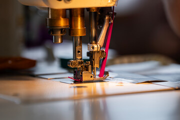 Zoom sur une machine à coudre en pleine action dans un atelier de couture, avec l’aiguille en mouvement sur un tissu, illustrant le travail de confection artisanale.