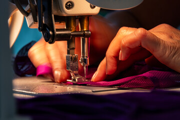Zoom sur une machine à coudre en fonctionnement avec des mains en pleine action guidant le tissu, illustrant le geste précis de la confection artisanale.