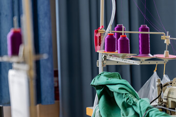 Gros plan sur des fils à coudre disposés sur un présentoir dans un atelier de couture, illustrant l’organisation et la diversité des matériaux.