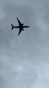 Vertical video of airplane flying across cloudy sky &ndash; dramatic upward view with clear silhouette of jet passing low and disappearing into distance. Perfect for travel, aviation, sky, and freedom theme