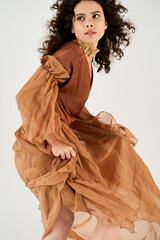Curly haired young woman exudes elegance in flowing dress within grey studio setting