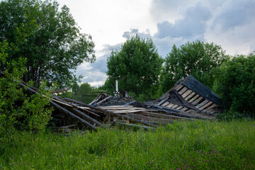 Destroyed wooden house crumbling in overgrown field with cloudy sky