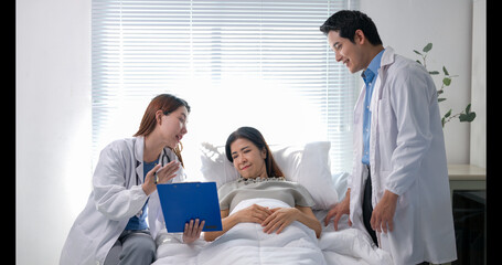 A woman is laying in a hospital bed with two doctors standing over her
