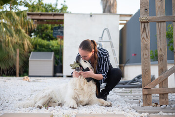 Woman kissing white big dog Golden Retriever holding toy in mouth on marble stones. Spending time with pet together outdoors