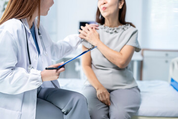A woman is sitting on a hospital bed while a doctor talks to her