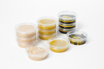 Assorted sauces in transparent plastic containers with lids on a white background. Includes light...