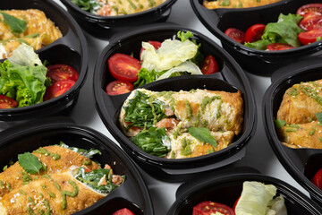 Omelette rolls with shrimp and red fish with herbs, served with salad mix and cherry tomatoes in black containers on a white background