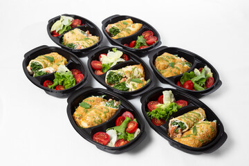 Omelette rolls with shrimp and red fish with herbs, served with salad mix and cherry tomatoes in black containers on a white background