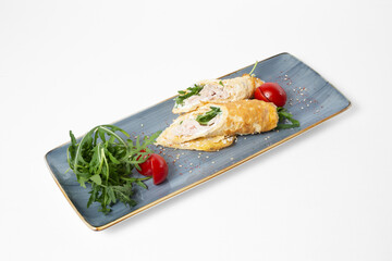 Omelette rolls with chicken and herbs, served with arugula and cherry tomatoes on a plate on a white background