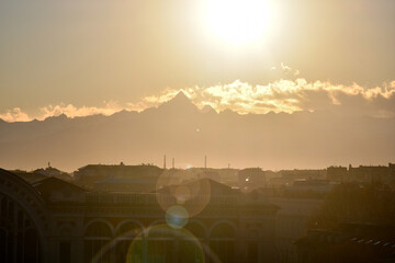 Backlight view with lens flares. Rooftops view of the old town with Alps mountain range and Monviso peak in the background at sunset, Turin, Piedmont, Italy