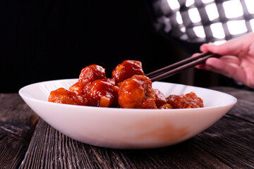 Meatballs with pineapple in sweet and sour sauce on wooden background. Chinese food. Asian cuisine