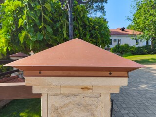A brown roof cap on a stone pillar. The roof cap is brown and has a triangular shape