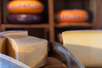 Blocks of cheese on wooden surface with cheese cutter on blurred background of several round,...