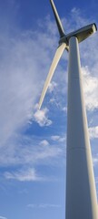 A wind turbine is tall and white, standing in the sky above a blue and cloudy day. Concept of power and energy, as well as the potential for renewable energy sources
