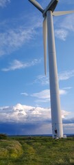 A wind turbine tower is tall and white, with a blue sky in the background. The scene is peaceful and serene, with a few people walking around the area